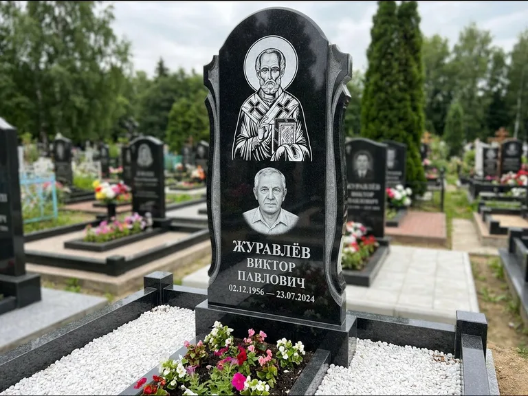 Памятник с гравировкой иконы: стела с образом в полный рост на обороте — гравировка образа Матроны Московской, низкие кусты спиреи в цвету, работа «Лебедева» в Тольятти